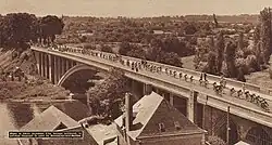 Photo en noir et blanc du peloton passant sur un pont au-dessus d'une rivière.
