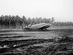Photographie noir et blanc d'un avion bimoteur sur une piste d'aviation en terre.