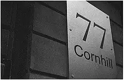 Sur un mur apparaît une plaque qui porte « 77 Cornhill ».