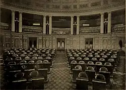 Illustration d'une assemblée avec un parterre de chaises devant une façade avec des piliers.