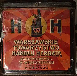 Une boîte rouge en métal sur laquelle est écrit "Warszawskie Towarzystwo Handlu Herbatą"