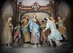 Photographie en couleurs. Groupe de statues colorées représentant les soldats en train de capturer Jésus. Le soldat au premier plan, de dos, à l'oreille coupée.