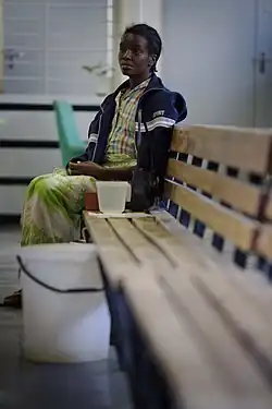 Photo d'une femme assise au bout d'un banc en bois qui attend, l'air résigné.
