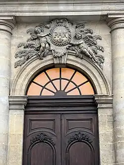 Détail de la porte d'entrée sur la place Monseigneur-des-Hameaux.