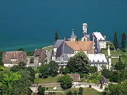 Photographie couleur d'un ensemble de bâtiments comportant une église, observés depuis un point haut, avec un lac en arrière-plan.