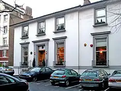 Photographie d'une façade d'immeuble claire avec des voitures garées au premier plan.