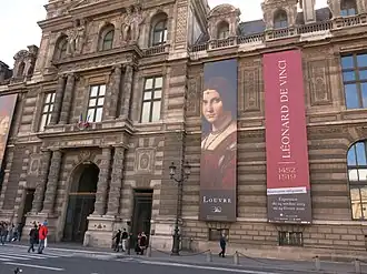 Photographie d'une façade d'un bâtiment classique portant de grands panneaux annonçant une exposition.