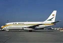 un avion Boeing blanc sur la tarmac avec l'inscription Air Mali et le drapeau malien en arrière