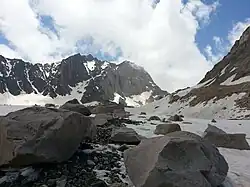 Blocs rocheux et cailloux reposant sur un glacier avec des montagnes en arrière-plan.