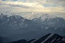 Des montagnes boisées en bas et enneigées plus haut, sous un ciel couvert.