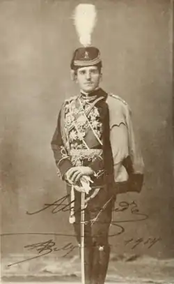 photographie noir et blanc : portrait d'homme en pied, en grand uniforme, appuyé sur un sabre, avec un shako à plumet