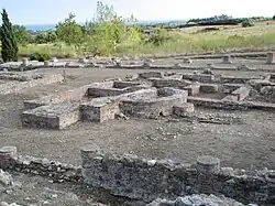 Vestiges de différentes constructions au sol avec des pieds de colonnes et des fondations de forme rectangulaire ou en demi-cercle.
