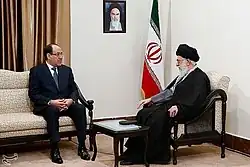 Deux homme assis en discussion, l'un en costume, l'autre en barbe blanche et turban