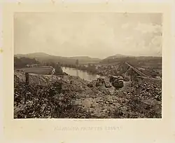 Photographie d'une rivière avec un pont ferroviaire et des arbres sur les rives.