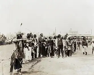 Photographie d'un groupe d'Amérindiens en habits traditionnels ou occidentaux tirant à l'arc