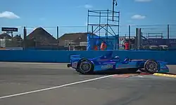 Photographie d'une monoplace de Formuel E bleu foncé, vue de profil, sur un vibreur, en ville.