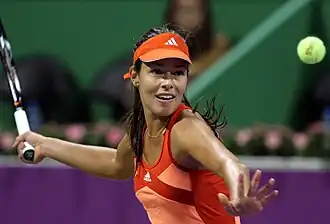 Une joueuse de tennis, concentrée, fixe la balle jaune des yeux, et prépare un coup droit.