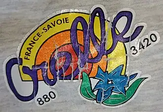 Photographie d'un logo de la commune d'Orelle avec du rouge, orange, jaune, vert et bleu, et l'inscription du nom de la commune en violet.