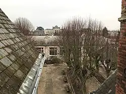 Photographie en couleurs d'une cour vue d'un toit la bordant, bordée d'une rangée d'arbres.