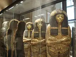 Sarcophages égyptiens disposés debout, derrière une vitrine.