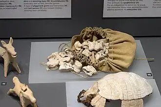 Jouets : figurines d’animaux, osselets (ἀστράγαλοι / astrágaloi), lyre en carapace de tortue.