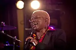 Portrait de 3/4 d'une chanteuse africaine aux cheveux cours teints en blong portant des lunettes en train de chanter