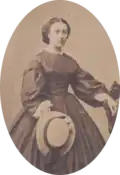 Photographie ancienne d'une femme en robe, tenant un chapeau de paille.