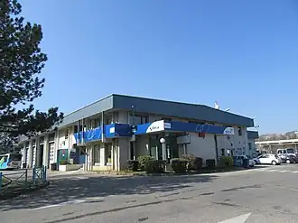 Photographie en couleurs d'un bâtiment à proximité duquel sont garés des bus et des voitures : le dépôt de la SIBRA à Annecy, également siège de l’entreprise.