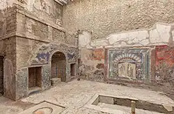 mur au fondcouvert de mosaïques colorés, à gauche niche arrondie. Devant, une grande banquette en U