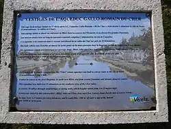 Vue d'une plaque explicative apposée à côté d'un vestige de monument antique.