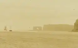 Photographie en sépia de l'arche des Kerguelen avant qu'elle ne s'effondre, avec deux navires à voile au mouillage à proximité
