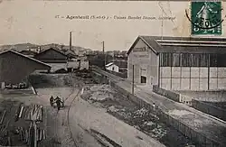 Carte postale représentant une cours d'usine traversée par une voie ferrée.