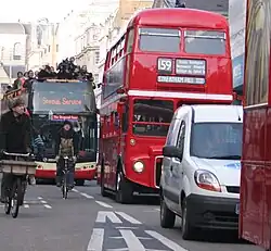 Photographie montant, dans une rue de Londres, une file de bus à impériale, doublés par des vélos.