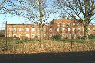 Derrière des arbres, un immeuble recouvert de briques rouges.