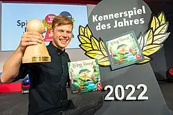 hauteur du jeu de société tenant le trophée et le jeu lors de sa victoire en 2022