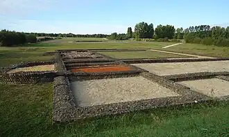 Photographie en couleurs de la base des murs d'un édifice antique divisé en plusieurs pièces.