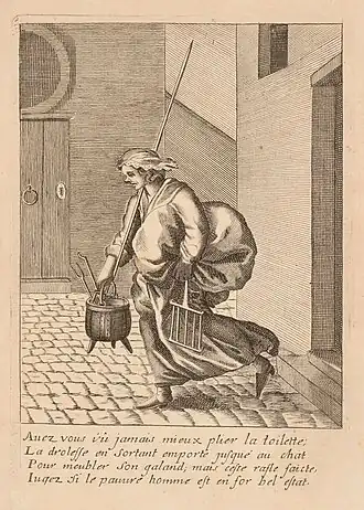 Une femme sort d'une maison dans la rue. Elle est chargée d'un gros ballot de tissus, d'une marmite, une fourche...
