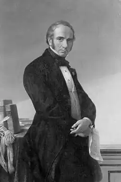 Le bourgmestre de Liège Louis Jamme, élégamment vêtu, pose de trois quarts. Il tient un papier de la main droite et est appuyé contre un meuble.