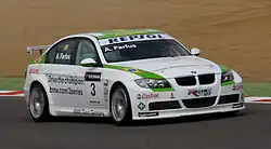 Voiture blanche à bandes latérales vertes, vue de trois-quarts, sur une piste sèche, en pleine ligne droite.