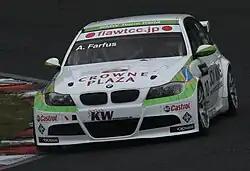 Voiture blanche à bandes vertes, de face, dans un virage, sur une piste sèche, malgré un ciel couvert.