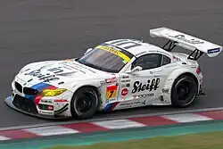 Photographie d'une voiture blanche, vue de trois-quarts, sur une piste sèche, en pleine ligne droite.