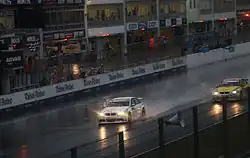 Sur piste très mouille et sous un ciel sombre, une voiture blanche passe la ligne d'arrivée.