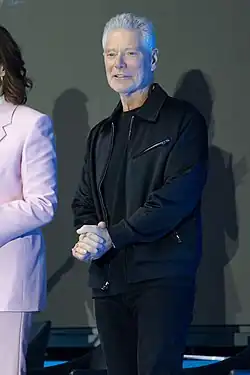 Homme aux cheveux blancs habillé en noir.