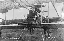 Photo noir et blanc, jeune homme présentant un biplan construit en bois toilé.
