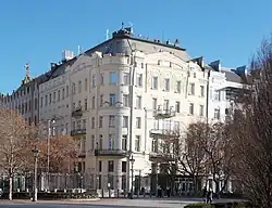 Photographie de l'angle d'un bâtiment en pierres couleur crème, où devant se trouve une rangée de grilles.