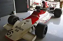 Photographie d'une monoplace de Formule 1 rouge et blanche, vue de trois-quarts dans un stand d'exposition.