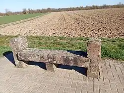 Photo d'un banc-reposoir en gré des Vosges, le banc est composé de cinq pierres, deux sur les coté servant de soutient dépassant les positions assises, une troisième servant de soutient aux deux dernières horizontales formant l'assise.