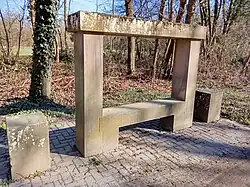 Photo d'un banc-reposoir en gré des Vosges disposant de deux traverses superposées, situé dans la forêt, l'ensemble parait relativement récent et à dont sans doute été réstauré.