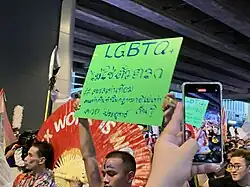 Pancarte tenue lors d'une marche où il est inscrit "LGBT" puis du texte en thaï