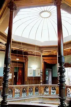 Espace octogonal avec portes et balustrades en bois. Verrière au plafond qui éclaire.